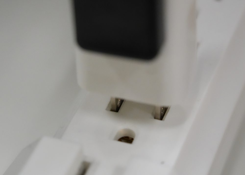 Close-up of a robot gripper inserting a plug into a wall outlet.